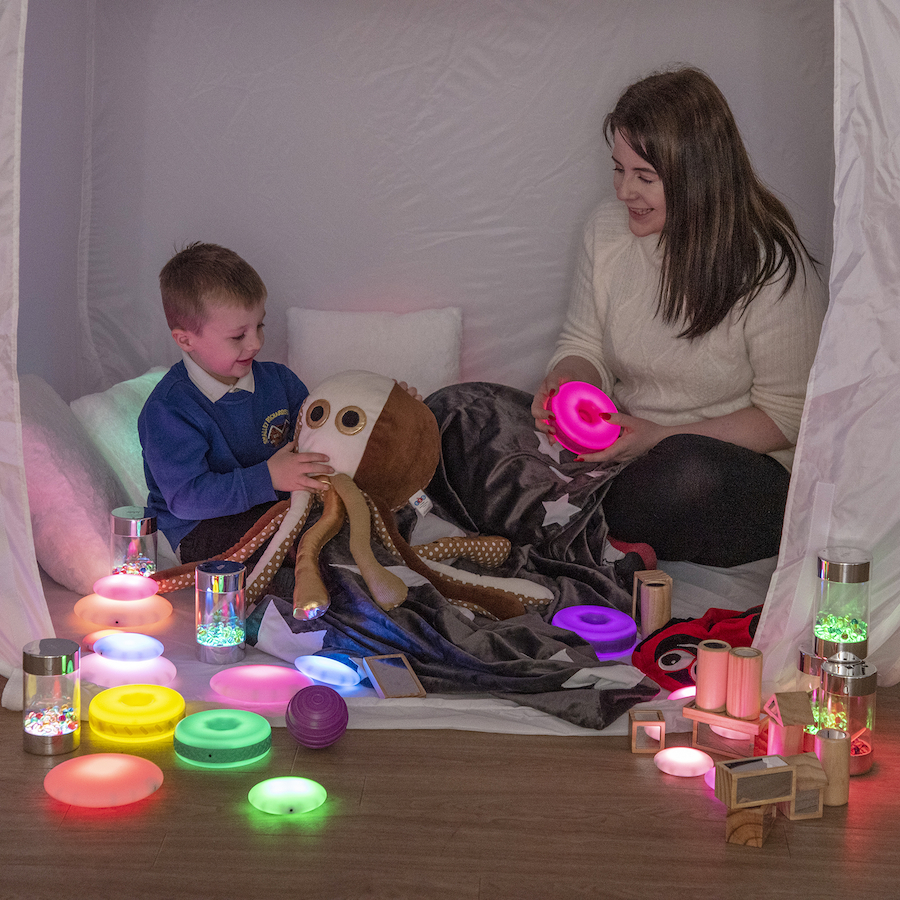 A woman and young boy play in dark den with light up toys