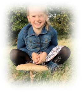 Young girl sat on grass crosslegged and smiling