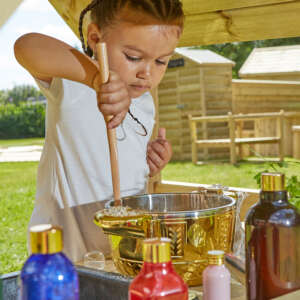 young chid mixing in an outdoor mud kitchen