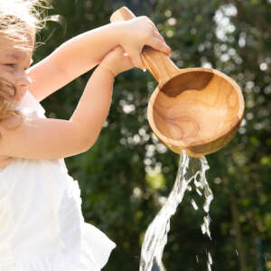 girl playing with water with a large wooden spoon
